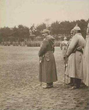 Parade im Westen: Kaiser Wilhelm II., König von Preußen im Gelände stehend, im Mantel, Pickelhaube, Säbel, begleitet von Offizieren, im Hintergrund Soldatenreihen