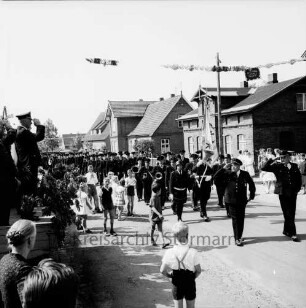 Mollhagen: Amtsfeuerwehrfest: Festumzug: Amtswehrführer Martin Haase und Ortswehrführer Hinrich Tretau salutieren vor Kreisbrandmeister Heinrich Harms und Ehrengästen: vorn und links Zuschauer: hinten Wohnhäuser und Bauernhäuser