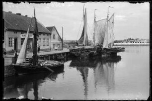 Kurisches Haff. Hafen mit Segelschiffen beladen mit Reet, im Hintergrund Tabakwarengeschäft "Bernhard Obersteller"