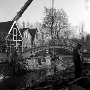 Trave: Stadtarm: Bau der Brücke zwischen der Hude und Heiligengeiststraße: ein Krangerät hebt die Brücke ein, vorne rechts eine Person, rechts Gebäude der Heiligengeiststraße, Blick nach Norden