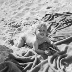 Kleinkind liegt auf einer Decke am Strand