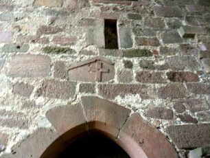 Langhaus (romanisch gegründet) im Nordnordwesten-vermauertes romanisches Tympanon über gotisch erneuerter Tür sowie darübiger Schießscharte