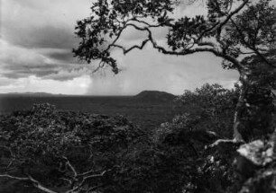 Hügellandschaft in Sambia : Blick auf die Hügel die Masevekette Sambias. Im Vordergrund eine bewaldete Ebene, mittendrin eine Bachaue. Am Horizont ein niedergehender Regenschauer.