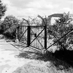 Glinde: Oher Weg: Gelände des ehemaligen Heereszeugamtes: vorn Metalltor mit Stacheldraht: rechts und links Büsche: hinten mehrere Hallen