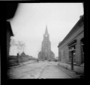 Vendin-le-Vieil (Dep. Pas-de-Calais, Frankreich): "Kirche von Alt-Vendin", im Vordergrund eine Straße mit einem zerstörten Gebäude (Rückansicht, Distanzaufnahme)