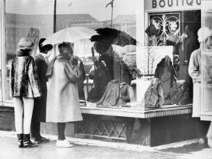 Einkaufsbummel. Frauen stehen vor einem Schaufenster einer Modeboutique und betrachten sich die Auslagen
