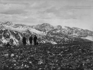 Bergpanorama : Eine Berglandschaft mit verschneiten Gebirgszügen im Hintergrund. Im Vordergrund sitzen drei Mitglieder des Transkontinentalen Geographenkongresses