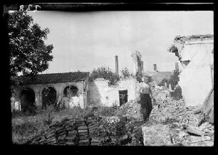 [Illies (?) (Dep. Nord, Frankreich)]: hemdsärmeliger Soldat zwischen Bruchsteinhaufen, im Hintergrund Gebäuderuinen
