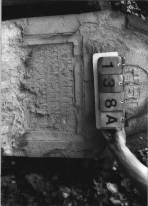 Grabstein 138 (Index: 100110695) Material: ? Zustand: untere Hälfte gänzlich verwittert, Abschieferungen im Giebel, sehr großer Textverlust Maße HxBxT: 122x77x14 cm Beschreibung: Stele, Rundbogenabschluß mit Ohren, Schriftfelder eingetieft Besonderheit: siehe freie Kommentierung: Grabstein 138A