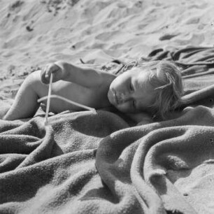 Kleinkind liegt auf einer Decke am Strand