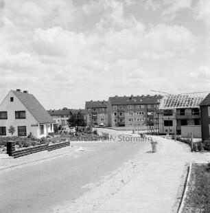 Hinschkoppel: Kellerberg-Süd: Neubaugebiet: links Einfamilienhaus mit Vorgarten: hinten Wohnblocks: rechts Wohnblock im Rohbau mit Gerüst: am Straßenrand Mülleimer