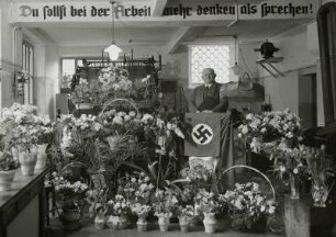 Roßwein, Druckereibesitzer Georg Liebe in der Druckerei inmitten von Blumenpräsenten zum 50jährigen Betriebsjubiläum an einem Pult mit Hakenkreuzfahne