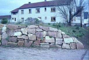 neue Trockenmauer aus Bruchsteinen vor einem Hang