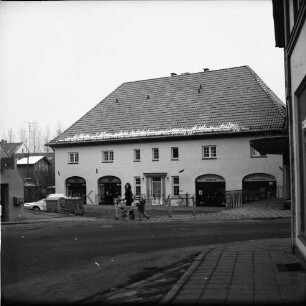 Hude: Blaues Haus: rechts Buchhandlung Willfang: links Mülltonnen und parkende Pkws: in der Mitte Frau mit Kinderwagen und Kind