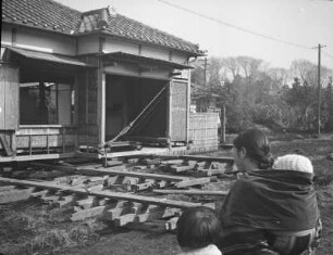 Ein japanisches Haus wird versetzt : Ein japanisches Haus wird versetzt. Ansicht mit Japanerin mit Kindern