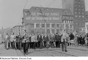 Männergruppe im Demonstrationszug beim Vorbeimarsch an der Ehrentribüne auf dem Karl-Marx-Platz (heute: Augustusplatz), im Hintergrund das Kroch-Hochhaus