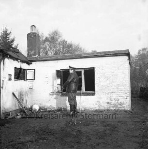 Brand: Sieker Landstraße: Behelfsheim: Brandruine mit eingestürztem Dach: davor Mitte Polizist: hinten Bäume