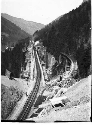 Aufgeschlitzter Teil des Ravennatunnels, neuer Viadukt mit darauf befindlichem Eisenbahnzug, gesprengter Westteil und noch nicht gesprengter Ostteil des alten Viaduktes