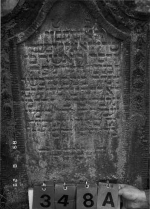 Grabstein 348 (Index: 100107792) Material: grauer Sandstein Zustand: stark verwittert, teilweise Textverlust Maße HxBxT: 104x57x9 cm Beschreibung: Stele, geschwungener Bogenabschluß, Schriftfeld eingetieft, Randfries mit Blüten Symbolik: Blütenfries: Grabstein 348A