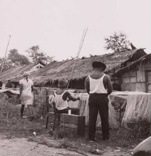 Kamerun. Fischer beim Netzflicken vor den Hütten eines Duala-Dorfes, um 1960