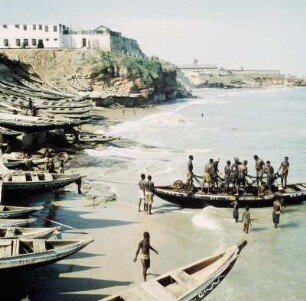 Accra. Ussher Fort : Accra (Ghana). Hasber Beach mit Ussher Fort, am Strand liegenden Surfboats und einem Boot, auf dem Männer Vorbereitungen zum Fischen treffen, 6. April 1959