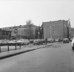 Hagenstraße: Parkplatz mit Pkws: in der Mitte Fußgänger: rechts Firmenschild der Volksbank Bad Oldesloe: hinten Rückfront des Stadthauses am Marktplatz