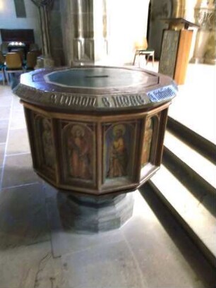 Stadtkirche-Langhaus Innen - Spätgotischer Taufstein unter dem Triumphbogen mit Umschrift sowie farbiger Darstellung der Heiligen in Ansicht von Süden
