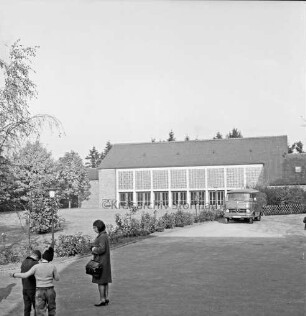 Volksschule: Soltausredder: vorn links zwei Schuljungen und Frau: dahinter Grünanlage mit Sträuchern und Bäumen: hinten Turnhalle: davor rechts Lieferwagen