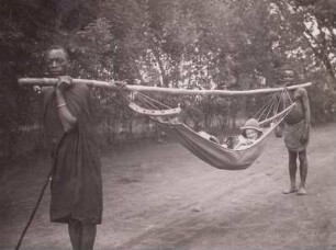 Lupembe, Deutsche Schule, Schülertransport : Tanganyika Territory (heute: Tansania). Lupembe, Deutsche Schule. Die einzige Tagesschülerin wird jeden Tag in einer Hängematte (machilla) zwei Stunden weit von Einheimischen zur Schule getragen, 1936