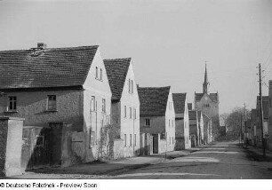 Blick in eine Dorfstraße, im Hintergrund eine Kirche