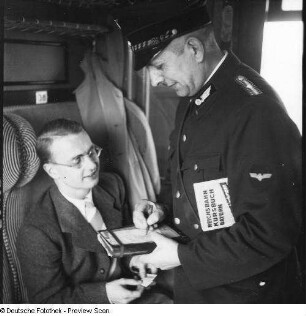 Zugführer der Deutschen Reichsbahn bei Fahrkartenkontrolle im Abteil eines Reisezuges