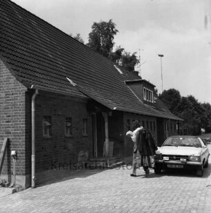 Polizei: Polizeistation im Rentnerwohnblock "Feierabendhaus": Papenwisch: vorn rechts Auffahrt mit Pkw: daneben Mann beim Transport von Kleidung: hinten rechts Bäume