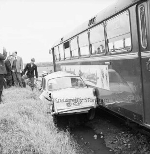 Bahnunfall: Eisenbahnstrecke der Elmshorn-Barmstedt-Oldesloe-Eisenbahn (EBOE): Bahnübergang Rümpeler Weg: Kollision eines Triebwagens mit einem Pkw: in der Mitte zwischen Bahndamm und Triebwagen eingeklemmter und zerquetschter Pkw: rechts Triebwagen: links Feuerwehrmann und Helfer