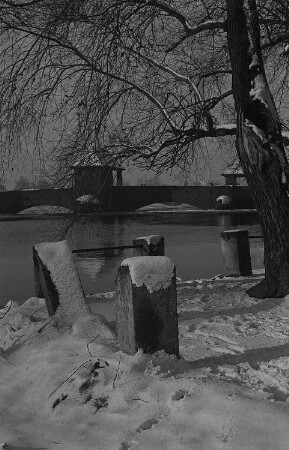 Parklandschaft im Winter mit Wasserlauf und Brücke
