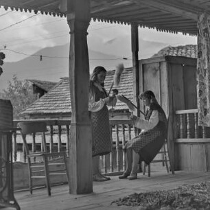 Veranda eines Wohnhauses in Bansko. Zwei junge Frauen in bulgarischer Tracht üben das Handwerk des Spinnens aus