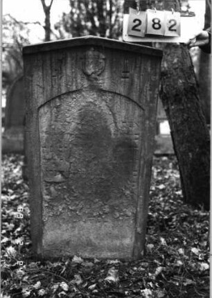 Grabstein 282 (Index: 99752232) Material: Sandstein Zustand: verwitt/abgeblätt. m. fast völl. Textverlus Maße HxBxT: 122x60x11 cm Beschreibung: Stele, giebelart. Abschl. m. Verdach. , Schriftfeld eingetieft m. Segmentbogenabschluß Symbolik: Urne: Grabstein 282