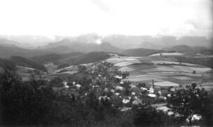Saupsdorf (Sebnitz-Saupsdorf). Ortsteilansicht mit Dorfkirche und Waldhufen. Blick vom Wachberg nach Südsüdwest gegen Hintere Sächsische Schweiz mit Raumberg und Winterbergmassiv bei Wolkentreiben