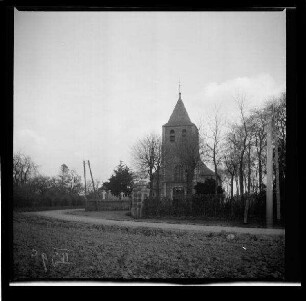 Wingles (Dep. Pas-de-Calais, Frankreich): "Kirche in Wingles" hinter Friedhofsmauer, im Vordergrund ein Feld (Rückansicht, Distanzaufnahme)