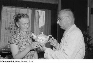 Kundin und Verkäufer betrachten eine Kanne am Stand der VEB Porzellanfabrik Freiberg, Herbstmesse 1953