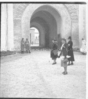 Touristinnen auf einem Platz in Casablanca, im Hintergrund Wachmänner in traditionellen Uniformen vor einem Torbogen, Marokko
