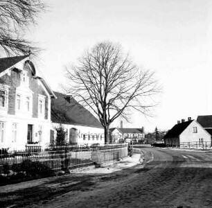 Dorfstraße mit Kopfsteinpflaster: links und hinten Bauernhäuser: davor Vorgarten mit Baum und Zaun: hinten Schornstein der Ziegelei: hinten rechts Haus: Winter