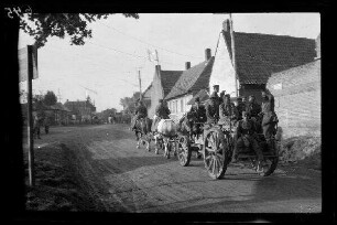 Bertincourt (?) (Dep. Pas-de-Calais, Frankreich): Offiziere oder Soldaten auf einem Leiterwagen und einem Vierspänner auf einer unbefestigten Ortsstraße (Rückansicht)