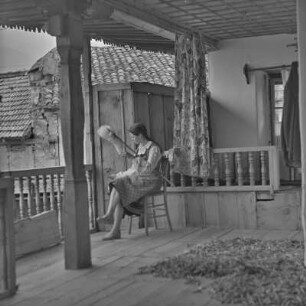 Veranda eines Wohnhauses in Bansko. Frau in bulgarischer Tracht übt das Handwerk des Spinnens aus