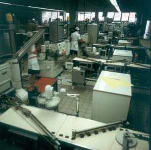 Blick in eine große Produktionshalle mit automatischen Formstraßen, Überzieh-und Füllanlagen, Kühlkanälen und Einwickelmaschinen