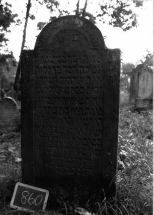 Grabstein 860 (Index: 100102959) Material: Sandstein Zustand: gut erhalten Maße HxBxT: 137x67x10 cm Beschreibung: Stele, eingezogener Rundbogenabschluss, Schriftfeld leicht eingetieft mit eingezogenen Ecken, im Oberrahmen Scheibenfries, zur Mitte in eine Blüte auslaufend Symbolik: Scheibenfries, Blüte: Grabstein 860