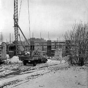 Bau eines Gebäudes: Rohbau mit Grundmauern und Gerüst: vorn Lkw: links Baubude, dahinter Kran: rechts Busch: Winter