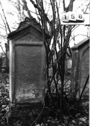 Grabstein 158 (Index: 99751987) Material: Sandstein Zustand: verwittert m. völl. Textverlust Maße HxBxT: 140x46x24 cm Beschreibung: Stele, Sockel, giebelart. Abschluß m. Verdach. u. Mittelakroter, rechteck. Schriftfeld Symbolik: Ranken: Grabstein 158
