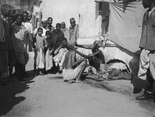 Bombay? (Indien). Straßenbarbier, umringt von Zuschauern, bei der Arbeit