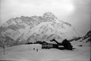Riezlern: Bauernhaus mit Bergen im Hintergrund, Gruppe Skiläufer