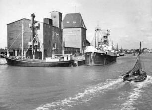 Büsum. Fischereihafen. Fischkutter und Frachtschiffe liegen am Pier. Im Hintergrund ein Lagerhaus